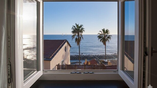 A room with a large window overlooking a beach with palm trees and a clear sky.