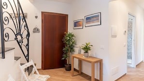 A hallway with a wooden door, a white chair, a small table with a plant, and two framed pictures on the wall.