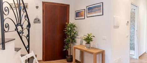 A hallway with a wooden door, a white chair, a small table with a plant, and two framed pictures on the wall.