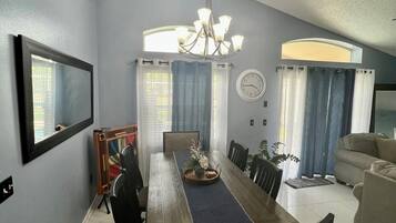 A dining area with a long wooden table, chairs, a chandelier, and a clock on the wall.