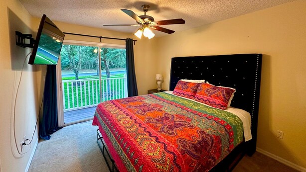 A bedroom with a bed, a ceiling fan, a TV mounted on the wall, and a view of a green lawn through a window. - Grand Superior 3BD Townhouse Near Disney 2 (Kissimmee)