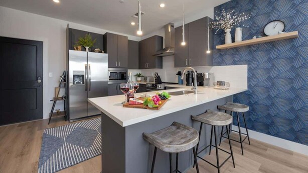 Une cuisine moderne avec un îlot central, des tabourets de bar et un mur orné d’un motif bleu.