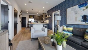 Un salon moderne avec un canapé, une table basse et un coin repas, la cuisine étant visible au fond.