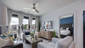 Une chambre d’hôtel moderne équipée d’un lit, d’un canapé, d’une table basse, d’une télévision et d’un balcon avec des rideaux.