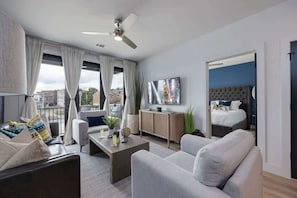 A modern hotel room with a bed, a sofa, a coffee table, a TV, and a balcony with curtains. - Parthenon Park-Odyssey-Heart of Midtown (Nashville)