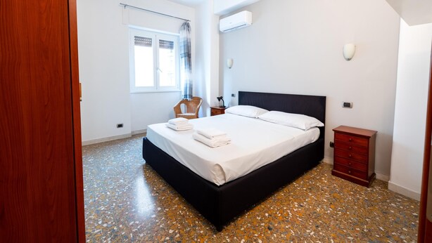 A bedroom with a large bed, a wooden dresser, a chair, and a window with a curtain. - Casa Di Cristina in Rome (Rome)