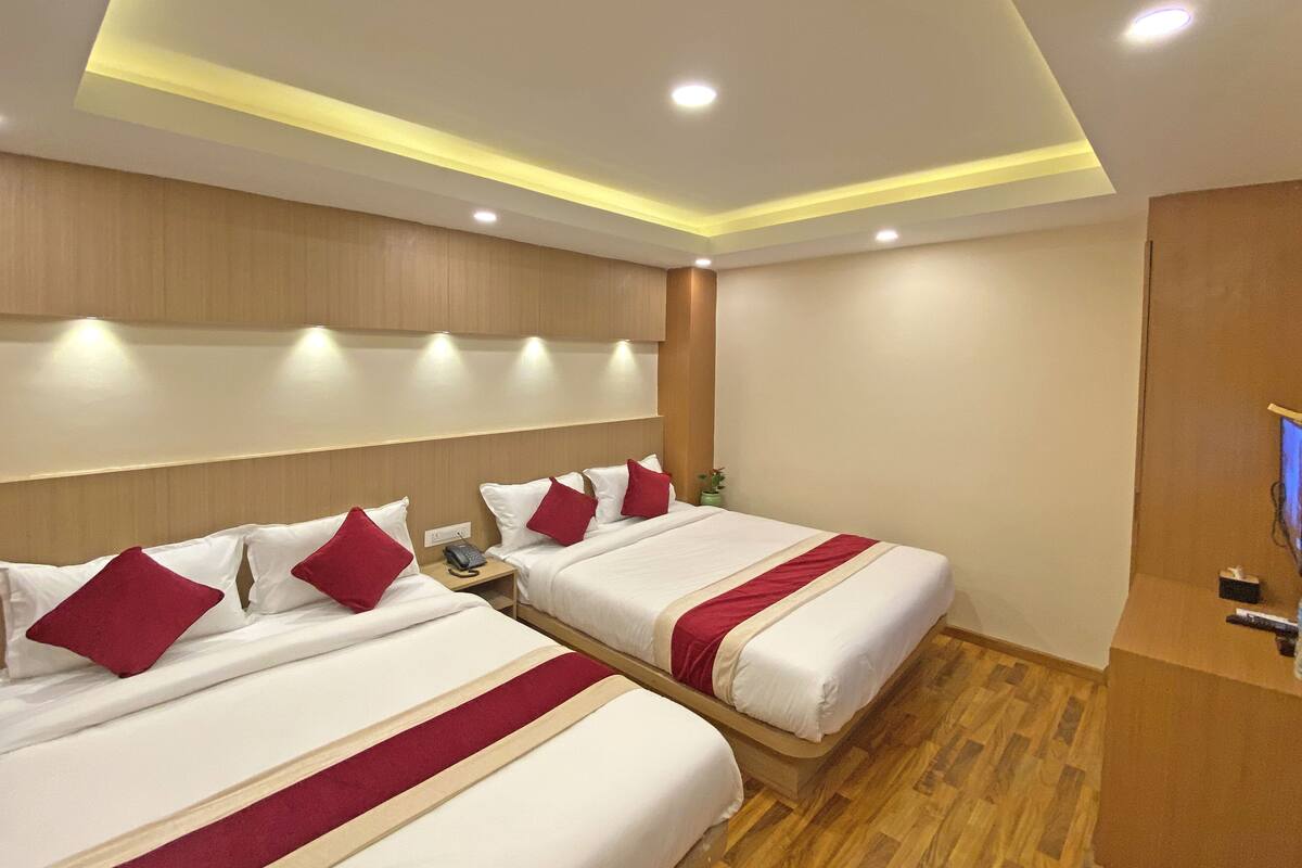 A hotel room with two beds, wooden headboards, recessed ceiling lighting, and a wooden floor.