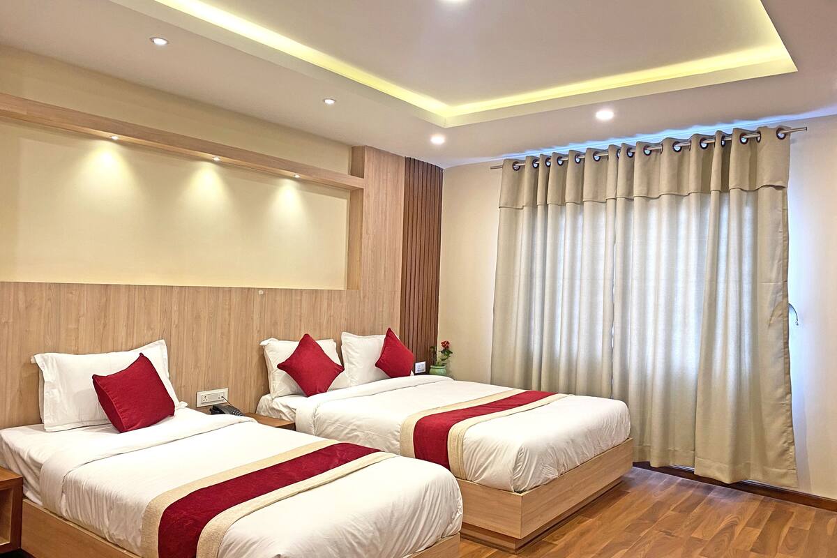 A hotel room with two beds, wooden headboards, a wooden floor, and a large window with curtains.