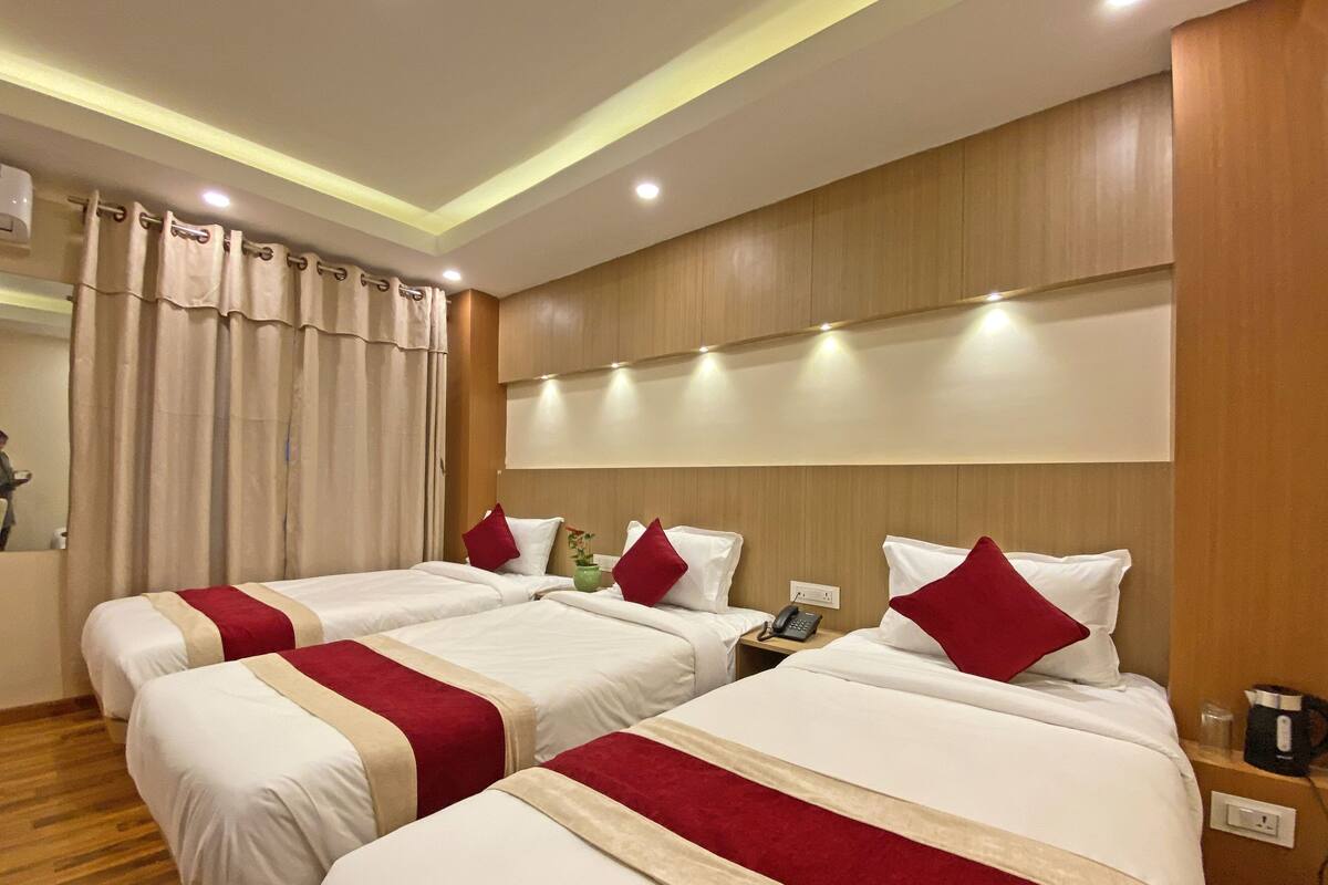 A hotel room with two beds, each with white bedding and red accents, a wooden headboard, and a bedside table with a phone and a kettle.