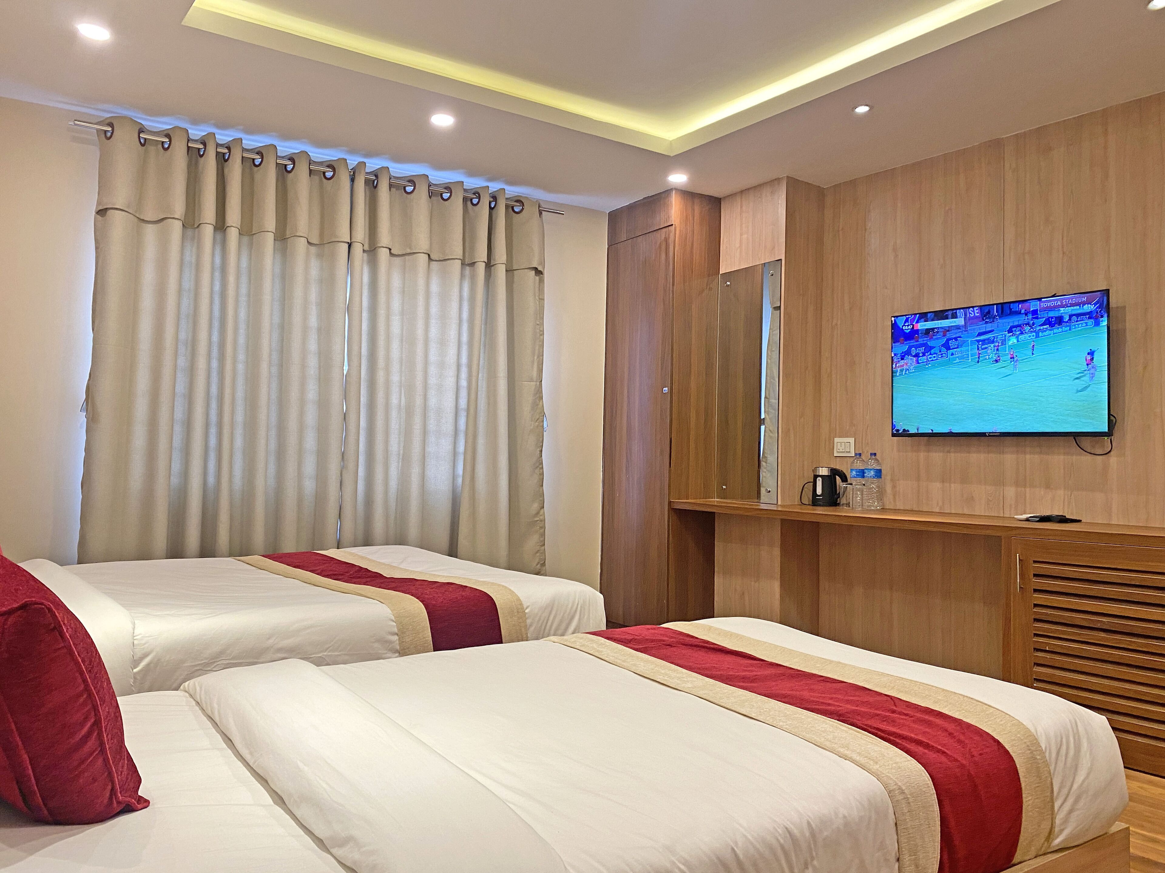 A hotel room with two beds, a TV, wooden paneling, and a window with curtains.