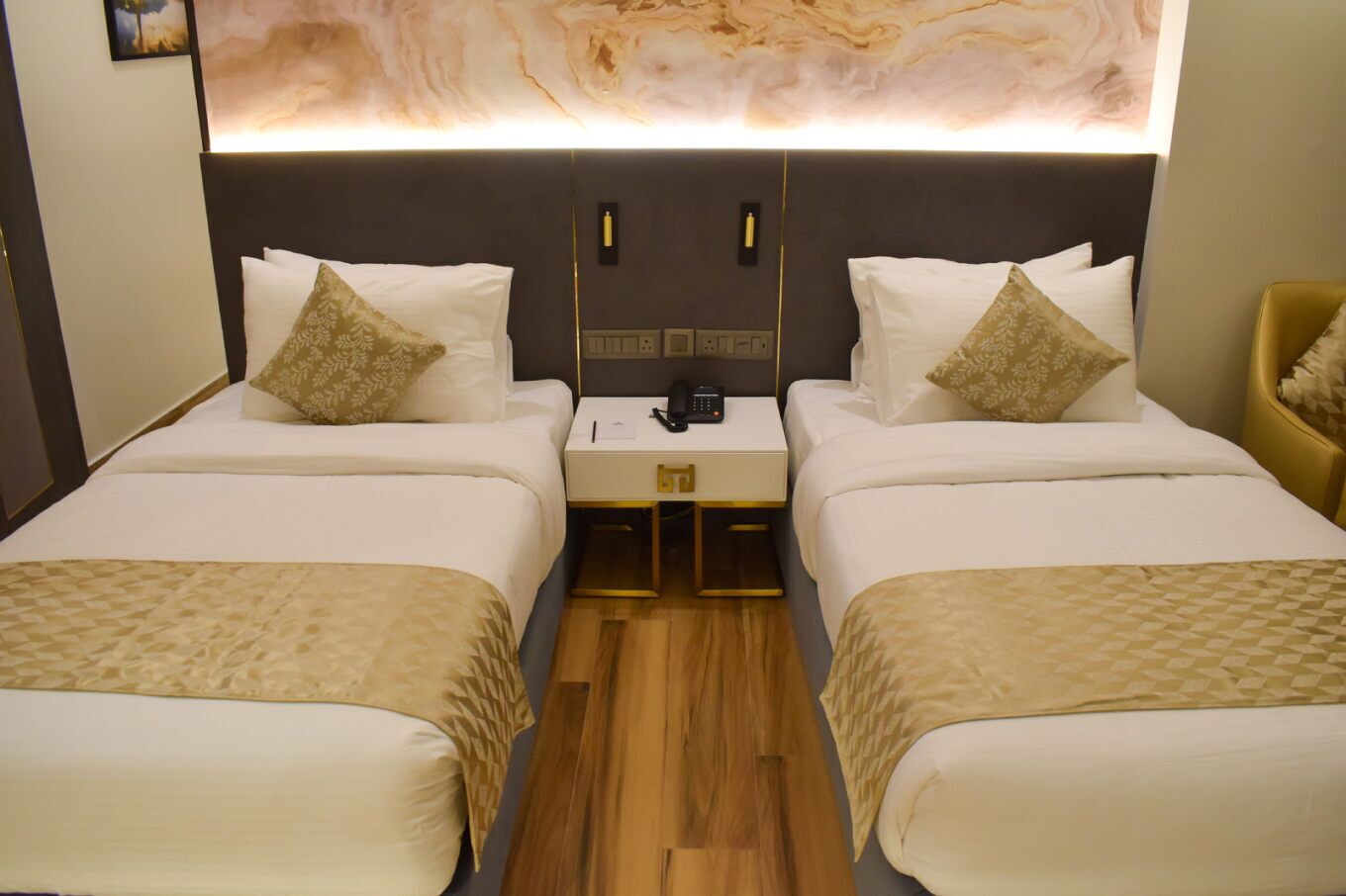 Une chambre d’hôtel avec deux lits, une table de chevet avec un téléphone et un mur décoré d’un motif imitant le marbre.