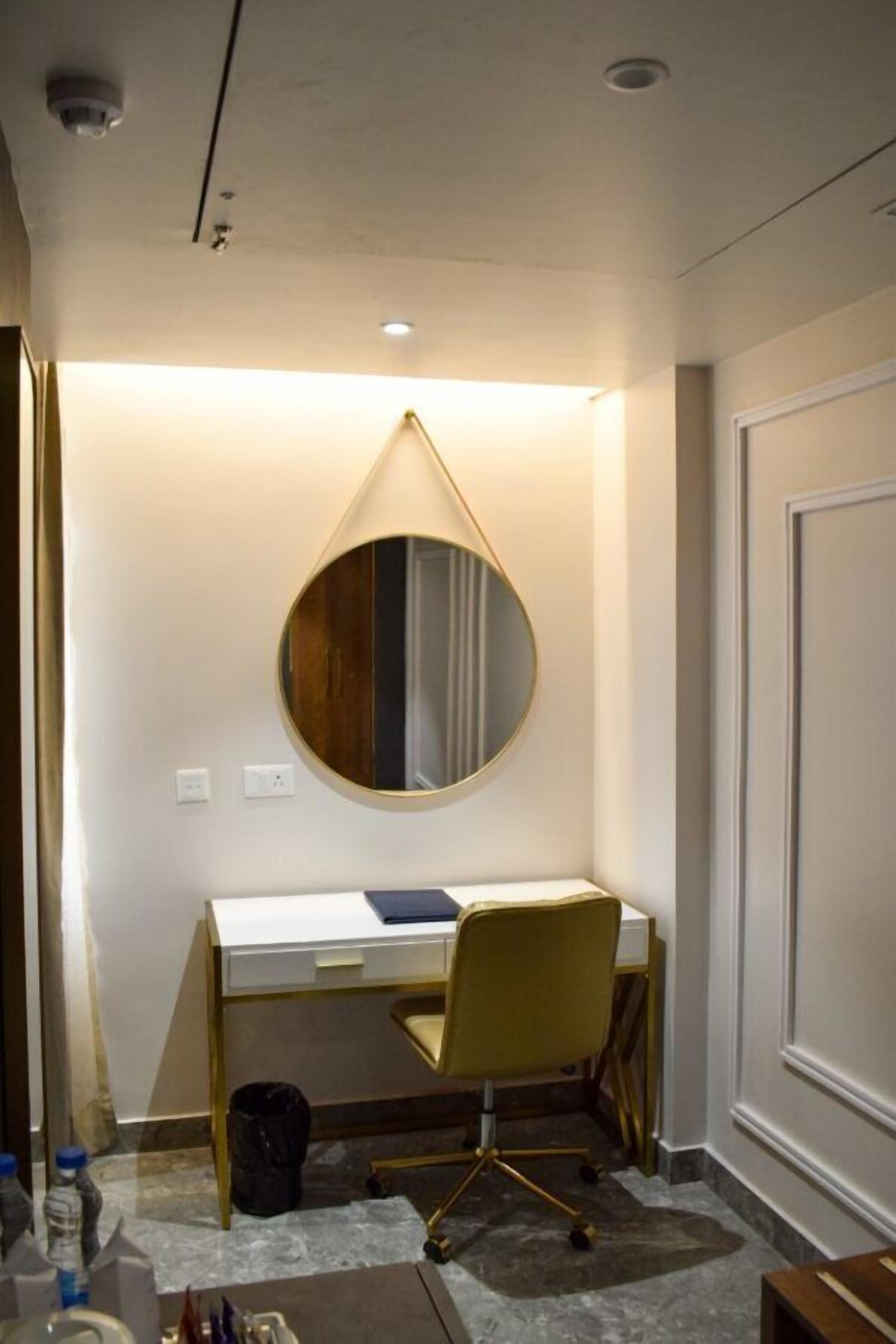 Habitación de hotel con escritorio, silla y un espejo redondo en la pared.