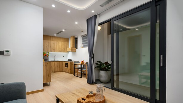 A modern living room with a wooden coffee table, a grey sofa, and a kitchen area in the background. - The Galaxy Home Apartment Doi Can (Hanoi)