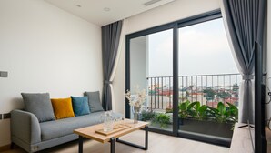 A modern living room with a grey sofa, a wooden coffee table, and a large window with a view of the city. - The Galaxy Home Apartment Doi Can (Hanoi)