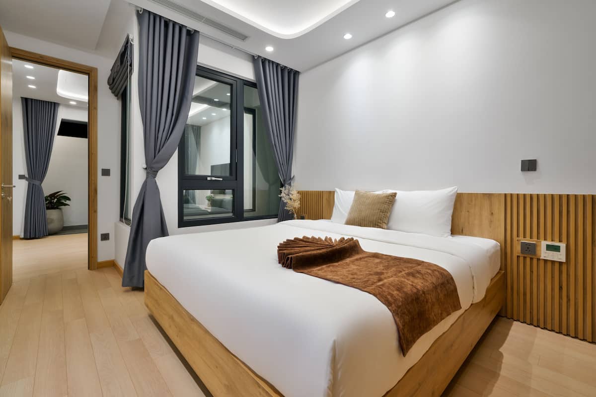 Une chambre d’hôtel moderne avec un grand lit, une tête de lit en bois et une vue sur la ville grâce à une grande fenêtre.