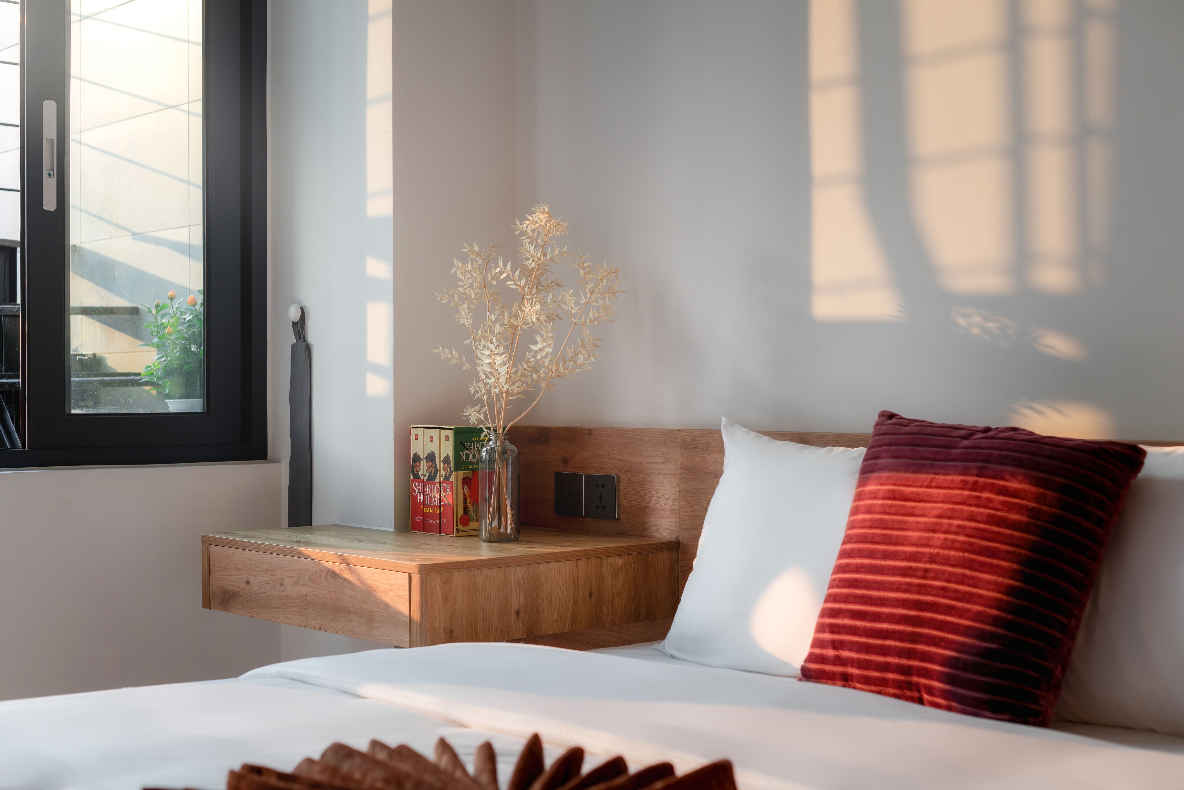 A bedroom with a bed, a nightstand, a window, and a vase with dried flowers.