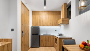A compact kitchen with wooden cabinetry, a built-in sink, and a dining area with a table and chairs. - The Galaxy Home Apartment Doi Can (Hanoi)