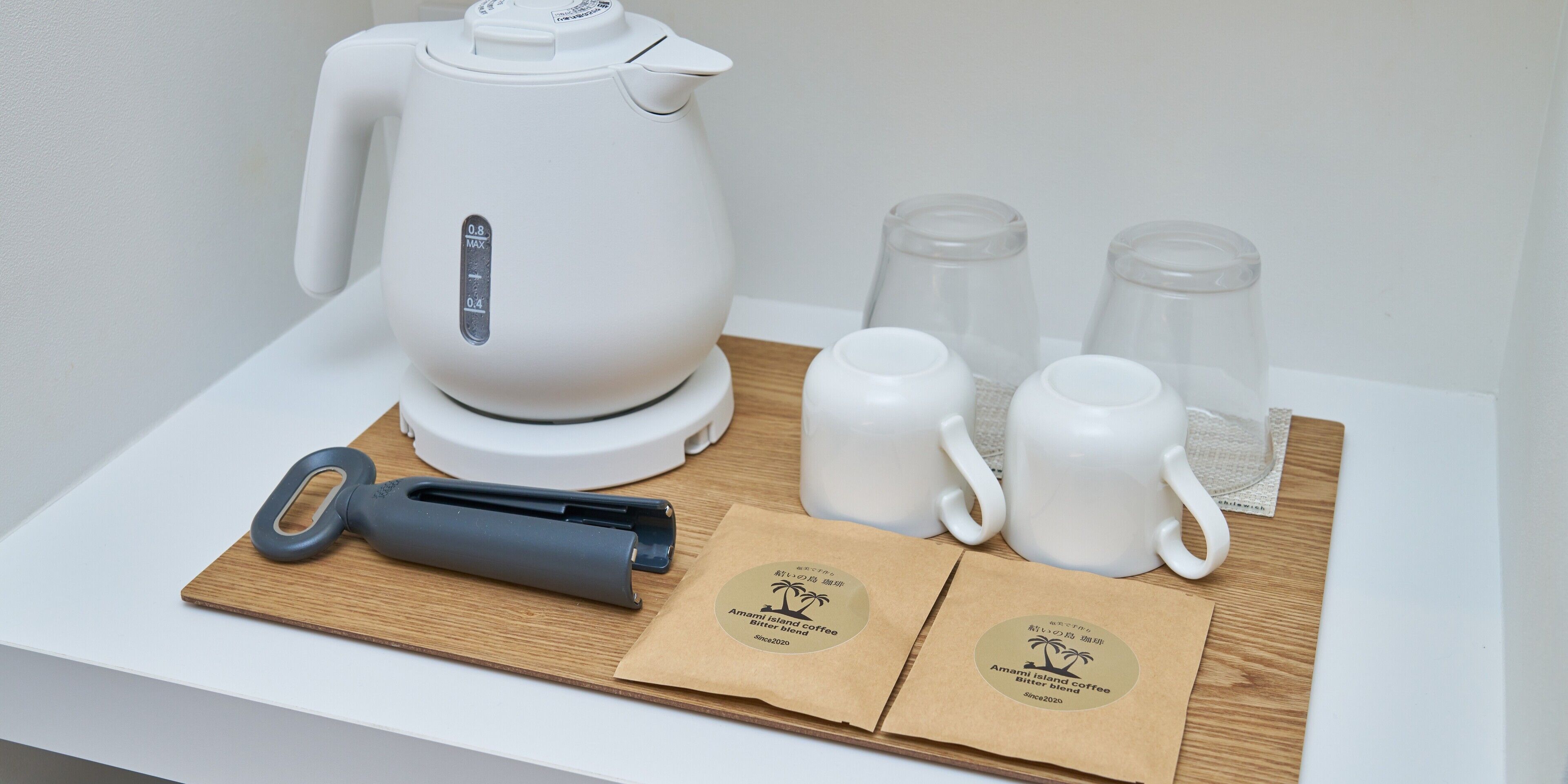 A coffee maker, two mugs, two glasses, a knife, and two coffee bags on a wooden tray.