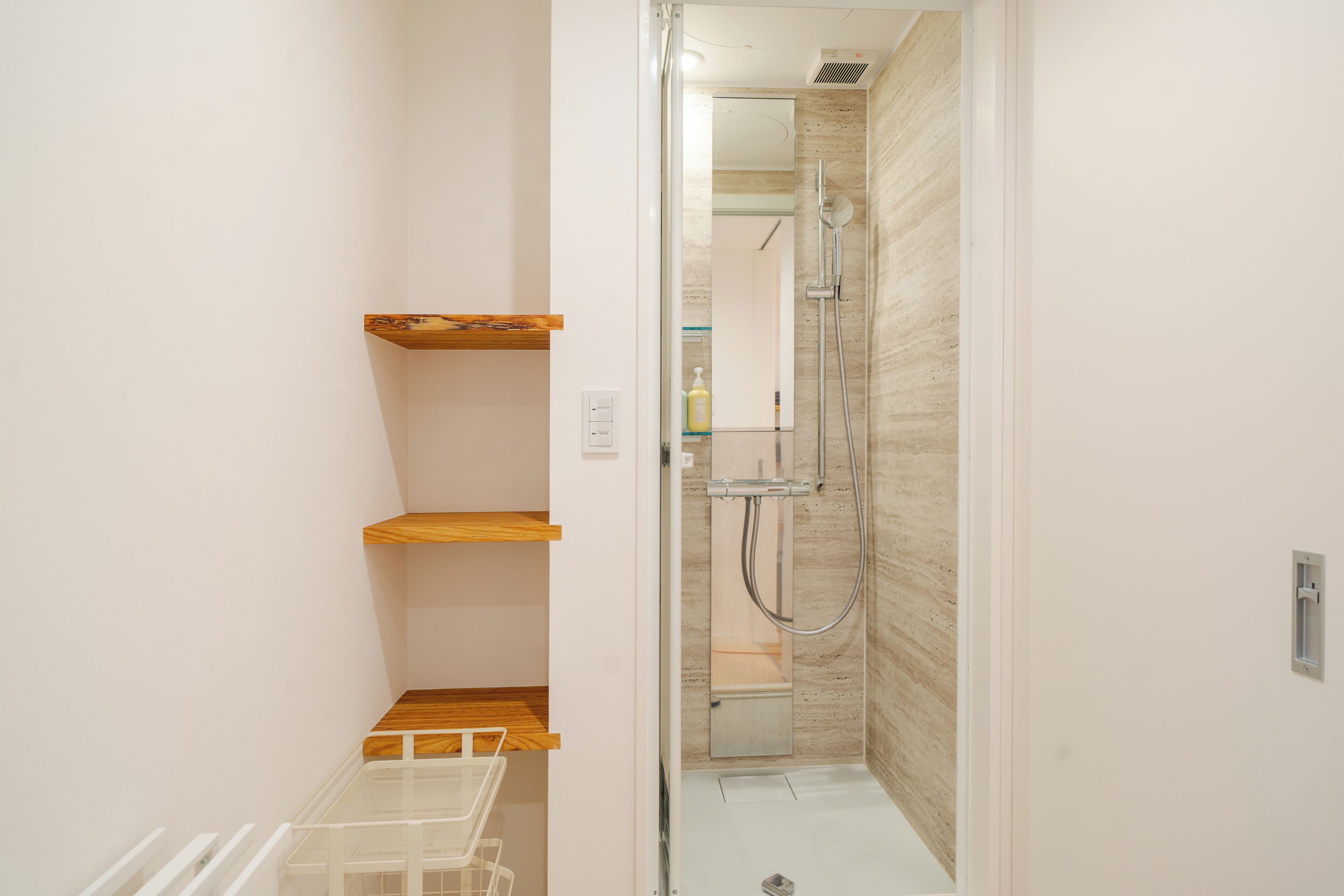A bathroom with a shower, wooden shelves, and a white sink.