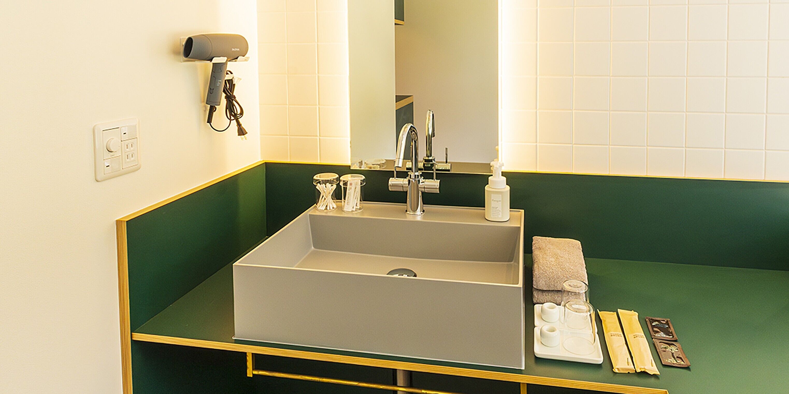 A bathroom with a large sink, a mirror, a hairdryer, and toiletries on the counter.
