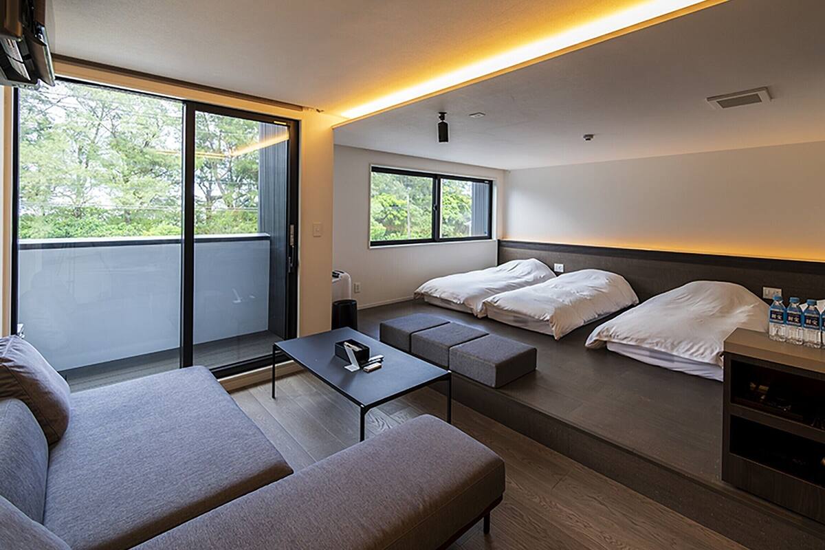 Una habitación de hotel moderna con un sofá, dos camas, una mesita y un televisor.