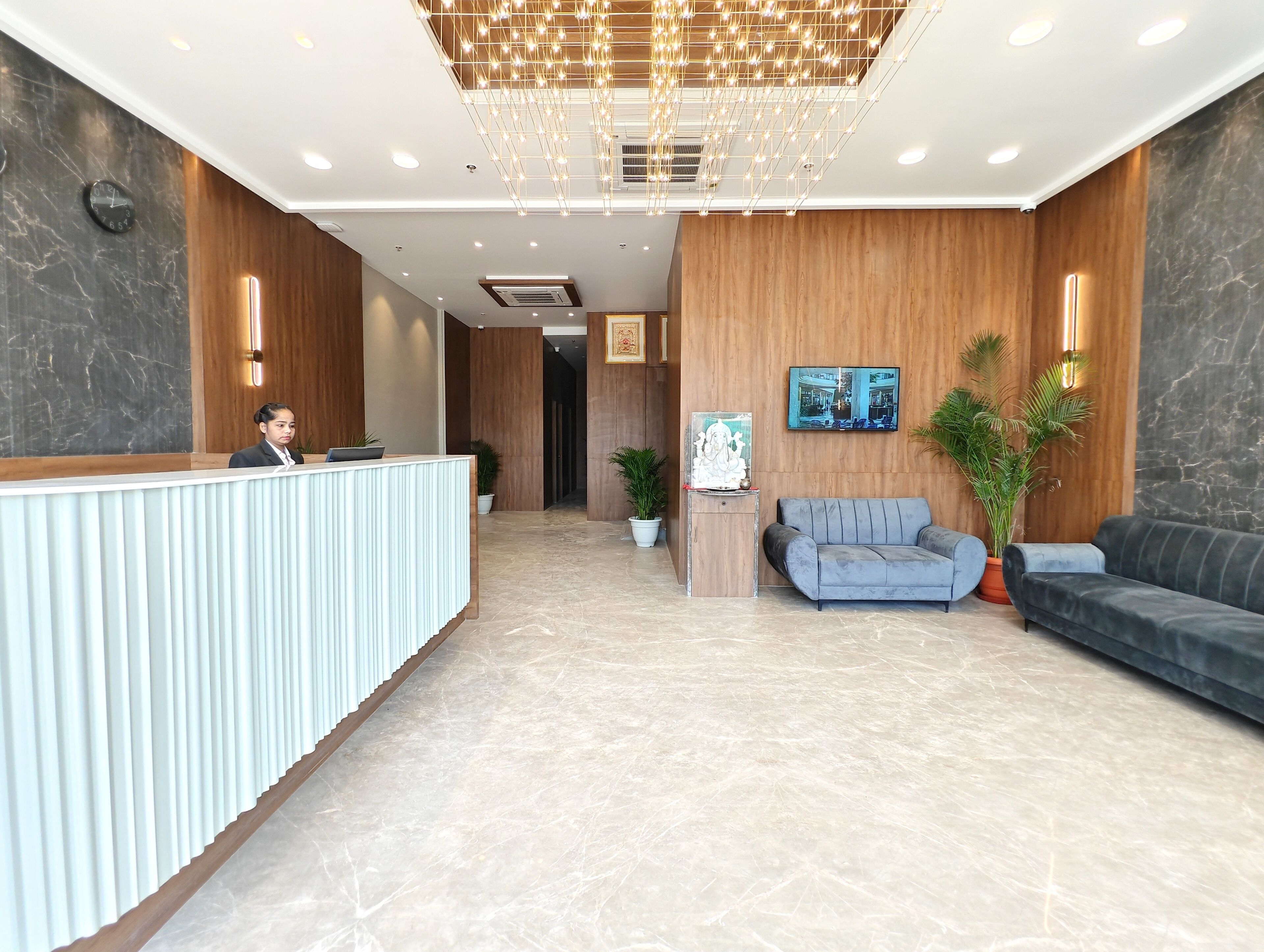 Un'area reception moderna con scrivania, una zona salotto con divani, una parete decorativa con un quadro incorniciato e una pianta in vaso.