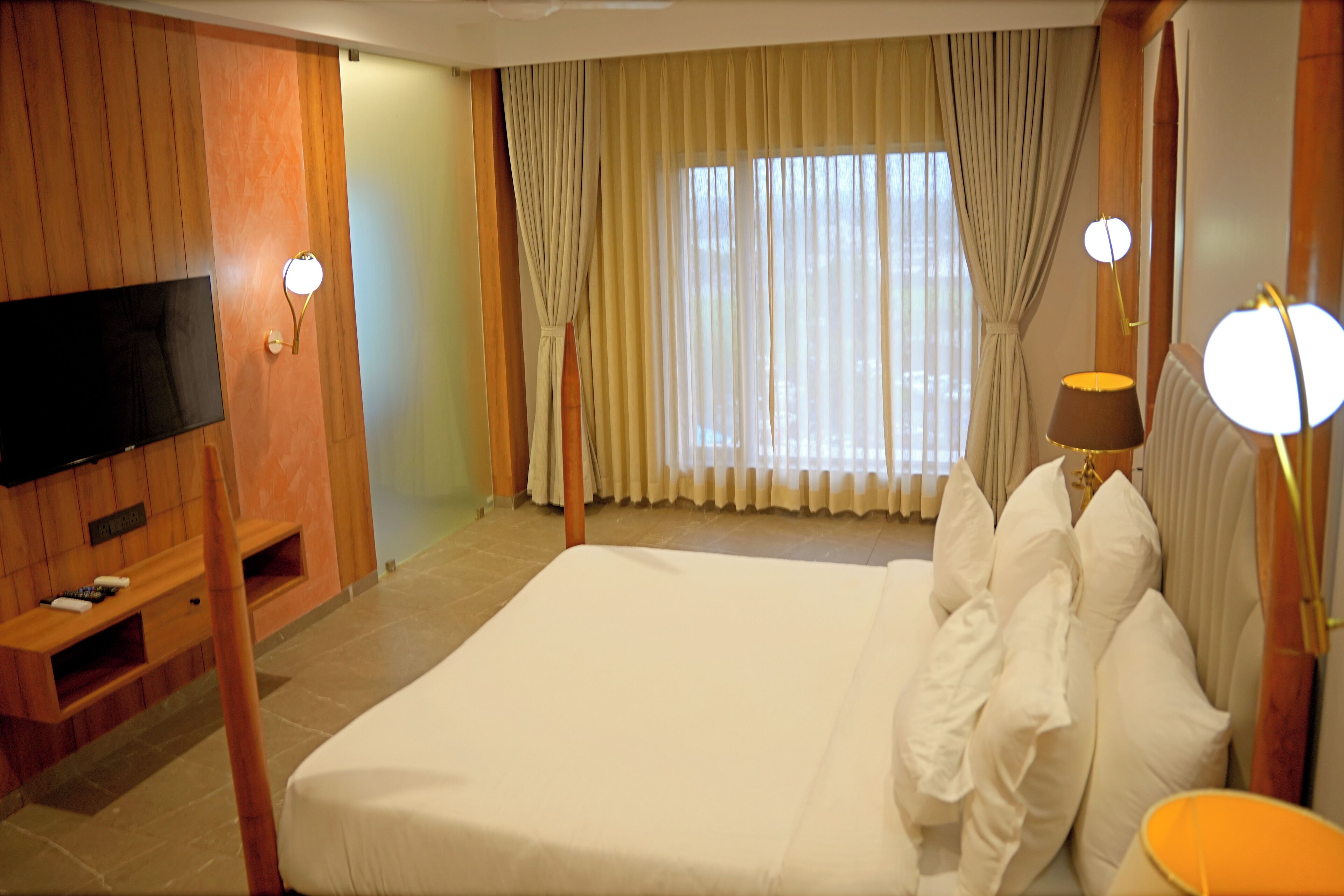 Habitación de hotel con una cama grande, paneles de madera, un televisor de pantalla plana y una ventana con cortinas.