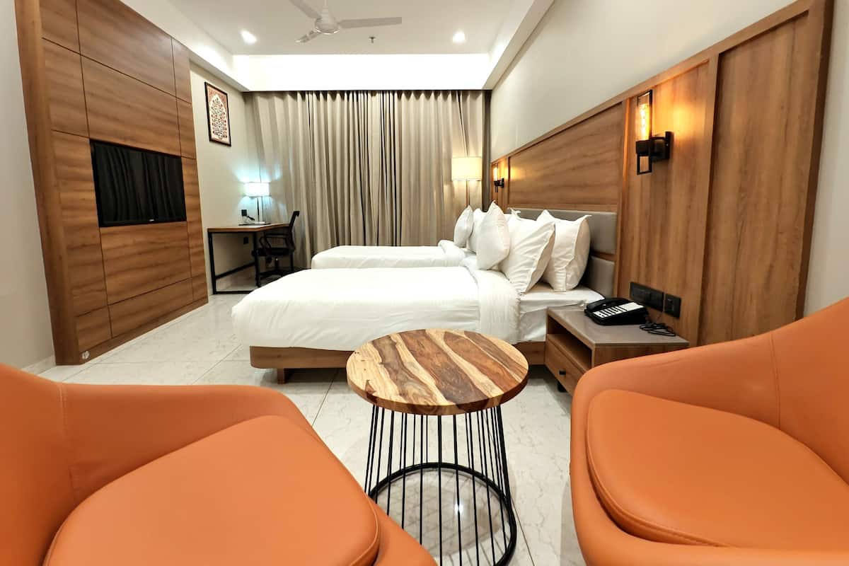 Ein Hotelzimmer mit zwei Betten, einem Schreibtisch, einem Sessel, einem runden Holztisch und orangenen Stühlen.