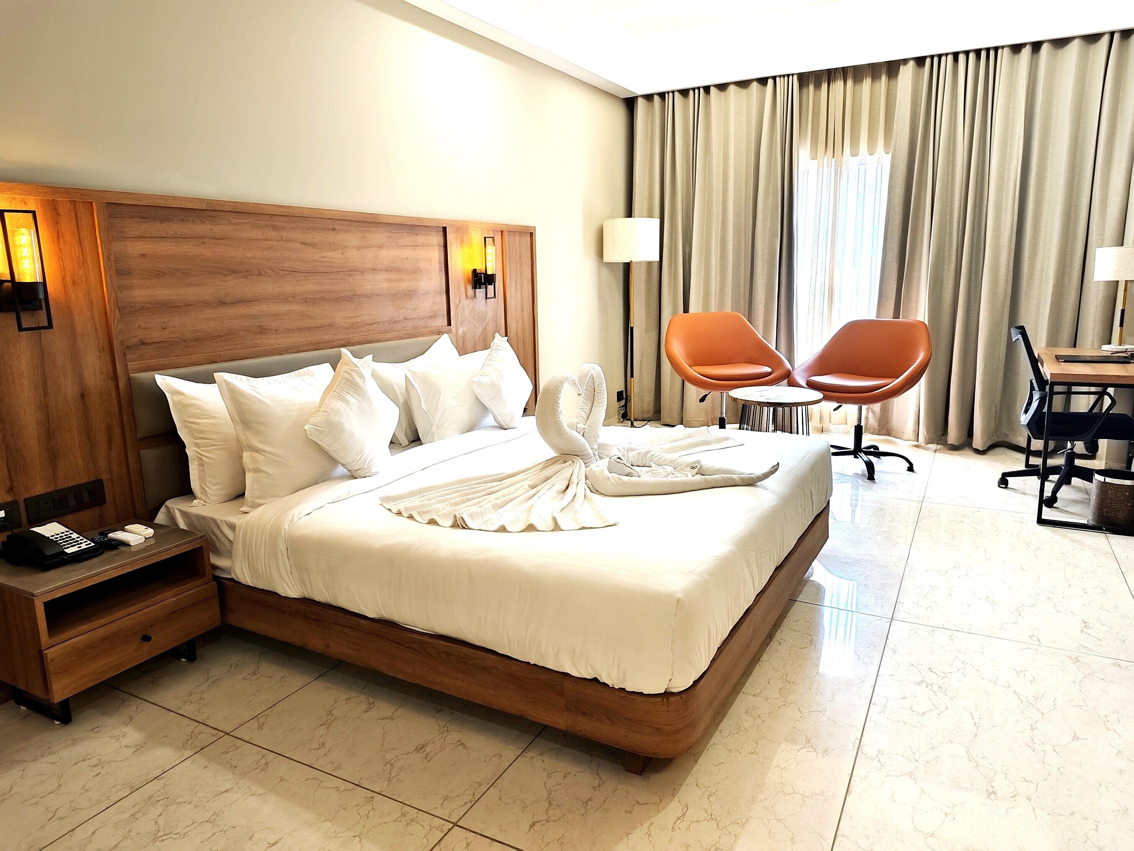 A hotel room with a large bed, two orange chairs, a desk, and a lamp.