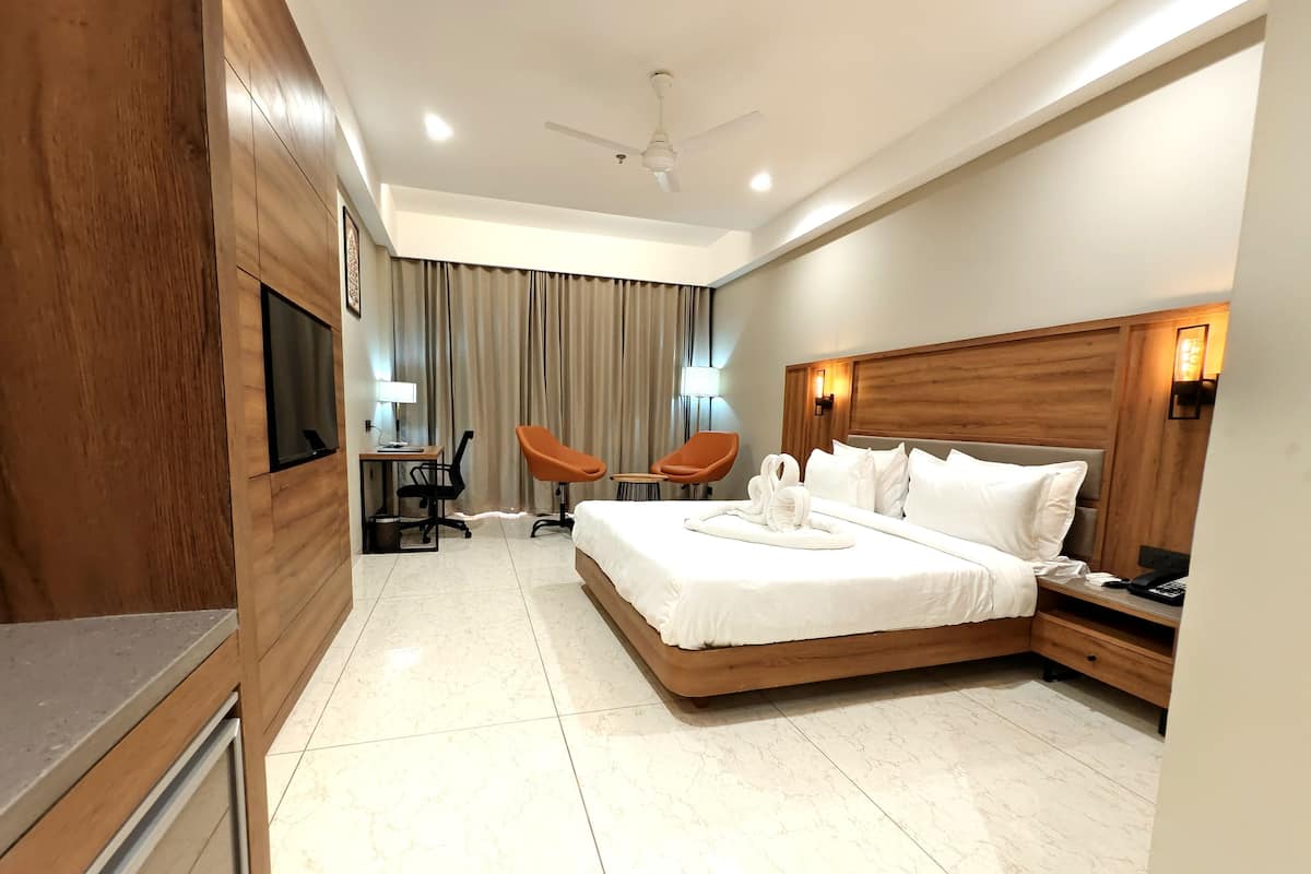 Ein Hotelzimmer mit einem großen Bett, einem Schreibtisch mit Stuhl, einem kleinen Tisch ebenfalls mit Stuhl und einem an der Wand befestigten Fernseher.