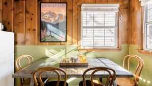 Un coin repas avec une table et des chaises en bois, une fenêtre avec des stores et une affiche représentant le lac Big Bear.