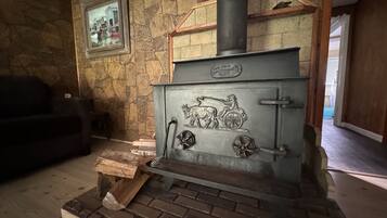 Un muro de piedra con un cuadro enmarcado, una estufa antigua con chimenea, y un banco de madera.
