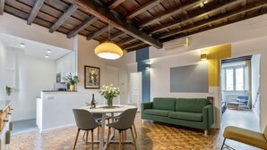 A modern living space with a wooden floor, a green sofa, a dining table with chairs, and a kitchen area in the background. - Santa Margherita Design Apartment in Navona (Roma)