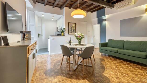 A modern kitchen with wooden flooring, a dining table with chairs, a green sofa, and a pendant light. - Santa Margherita Design Apartment in Navona (Roma)