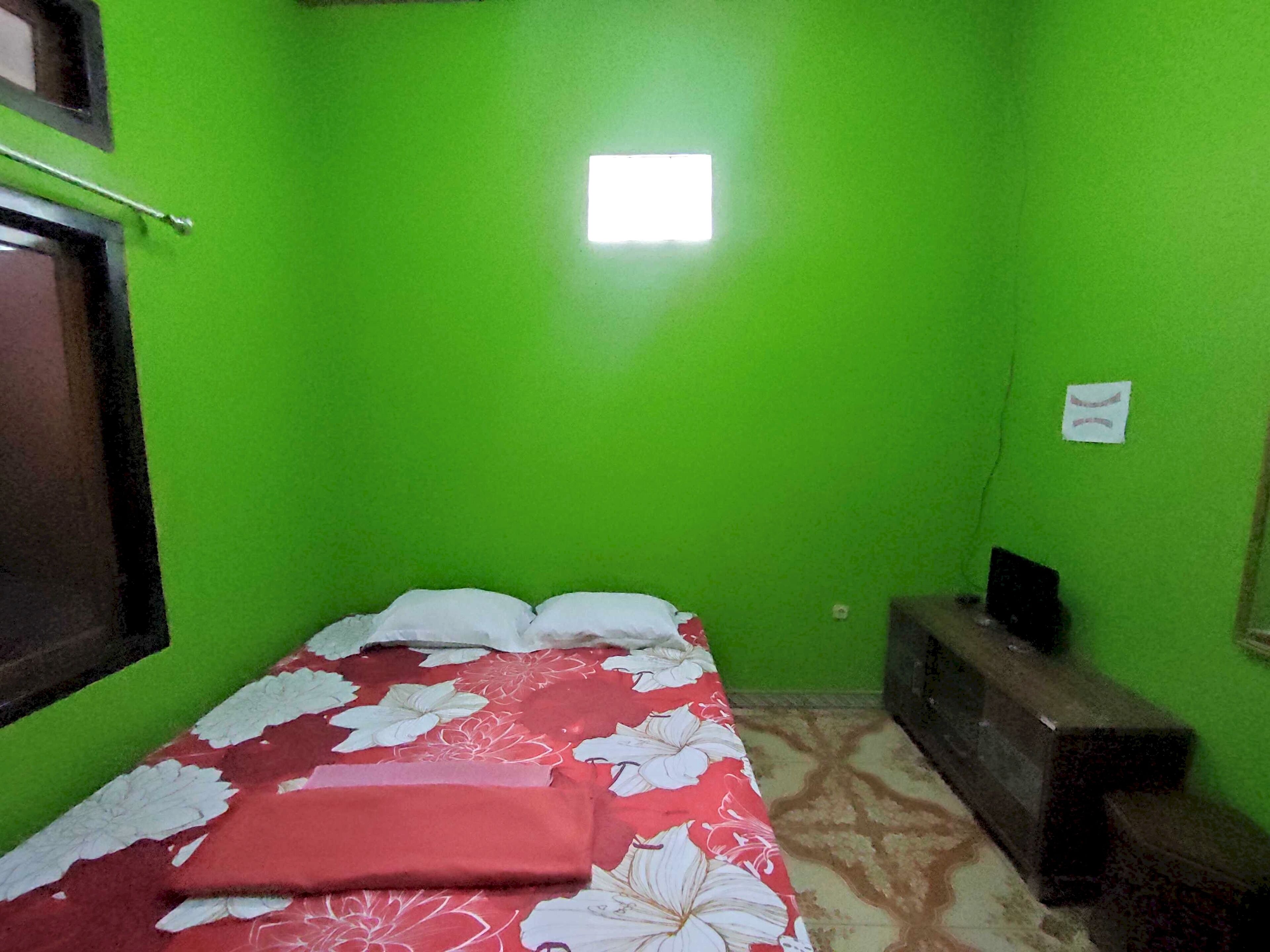A small, green-walled room with a bed, a small table, and a window.