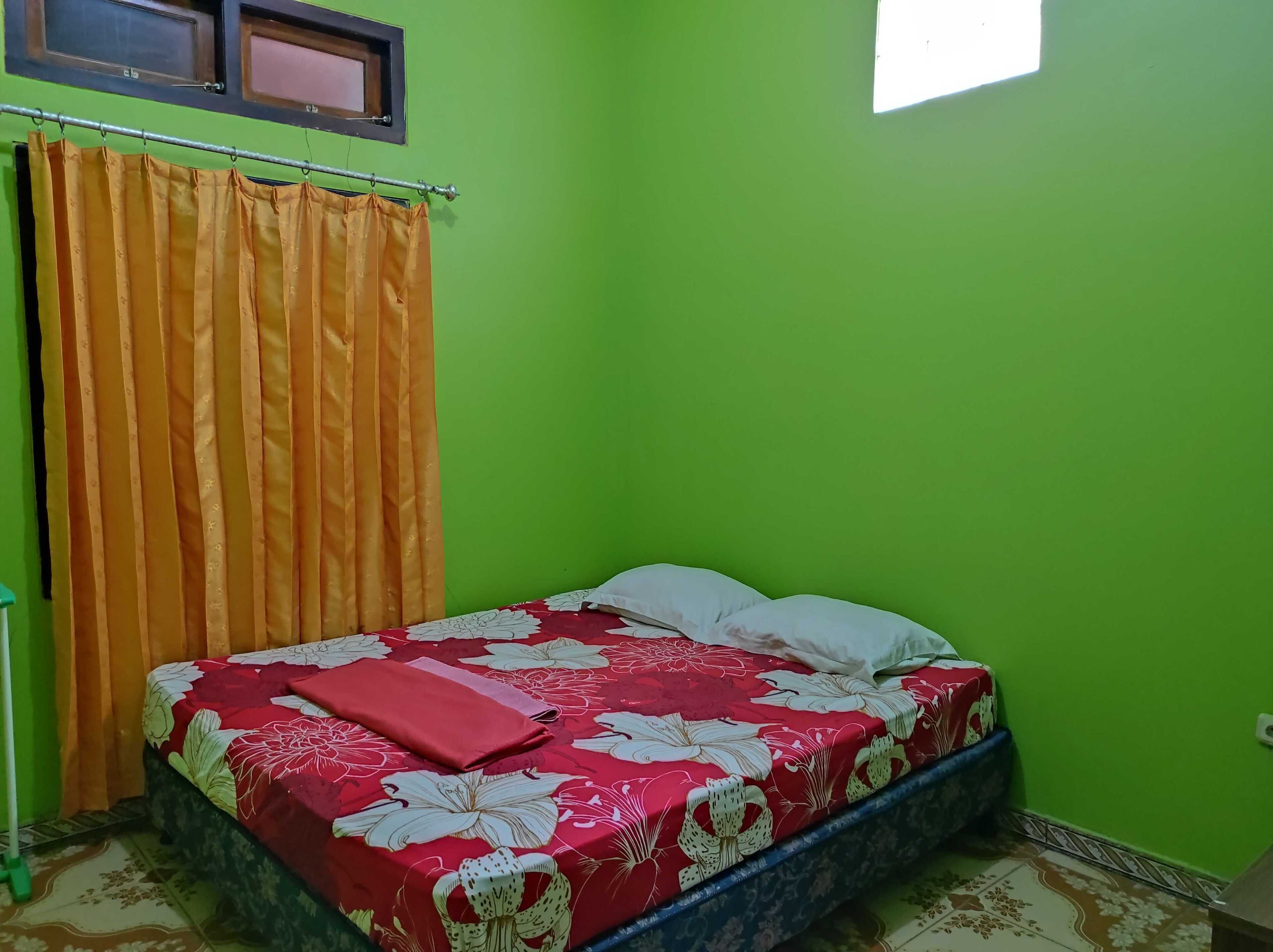 Una habitación pequeña con una cama, cortinas naranjas y paredes verdes.