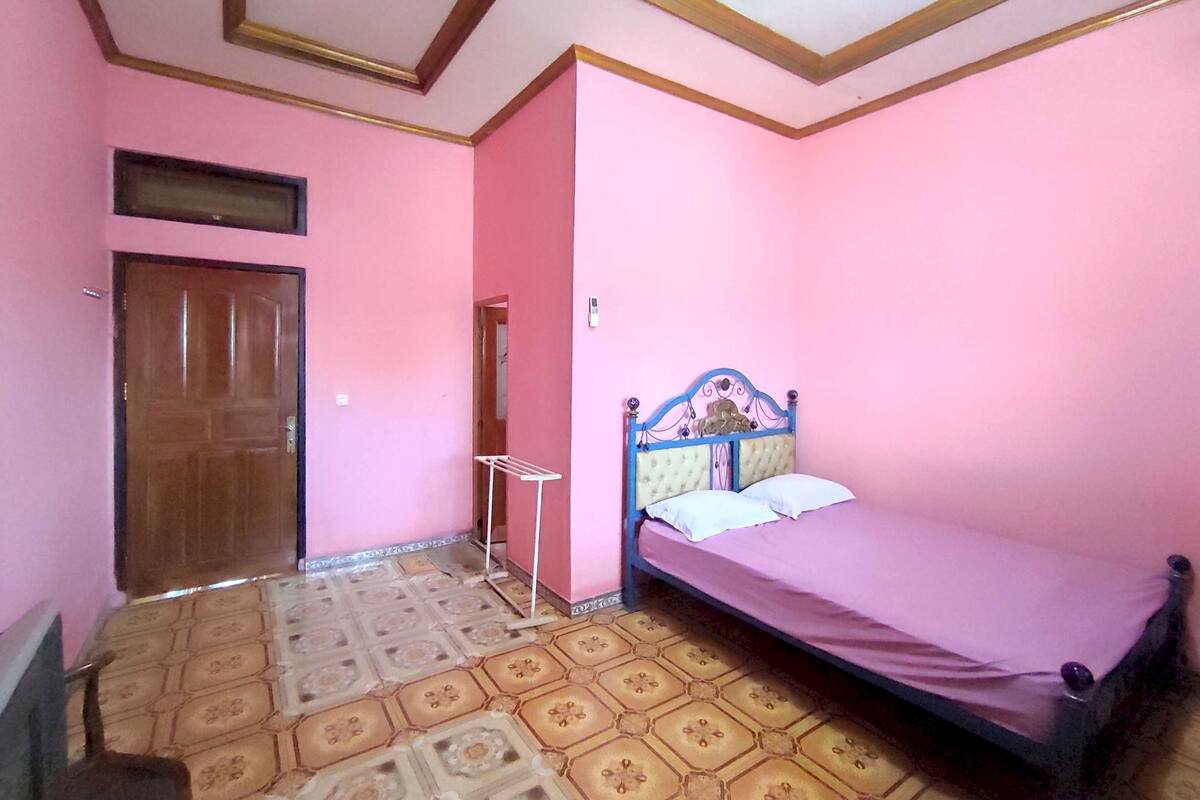 A bedroom with pink walls, a wooden door, a bed with a blue headboard, and patterned flooring.