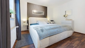 A modern bedroom with a bed, bedside tables, a mirror, and a dresser.