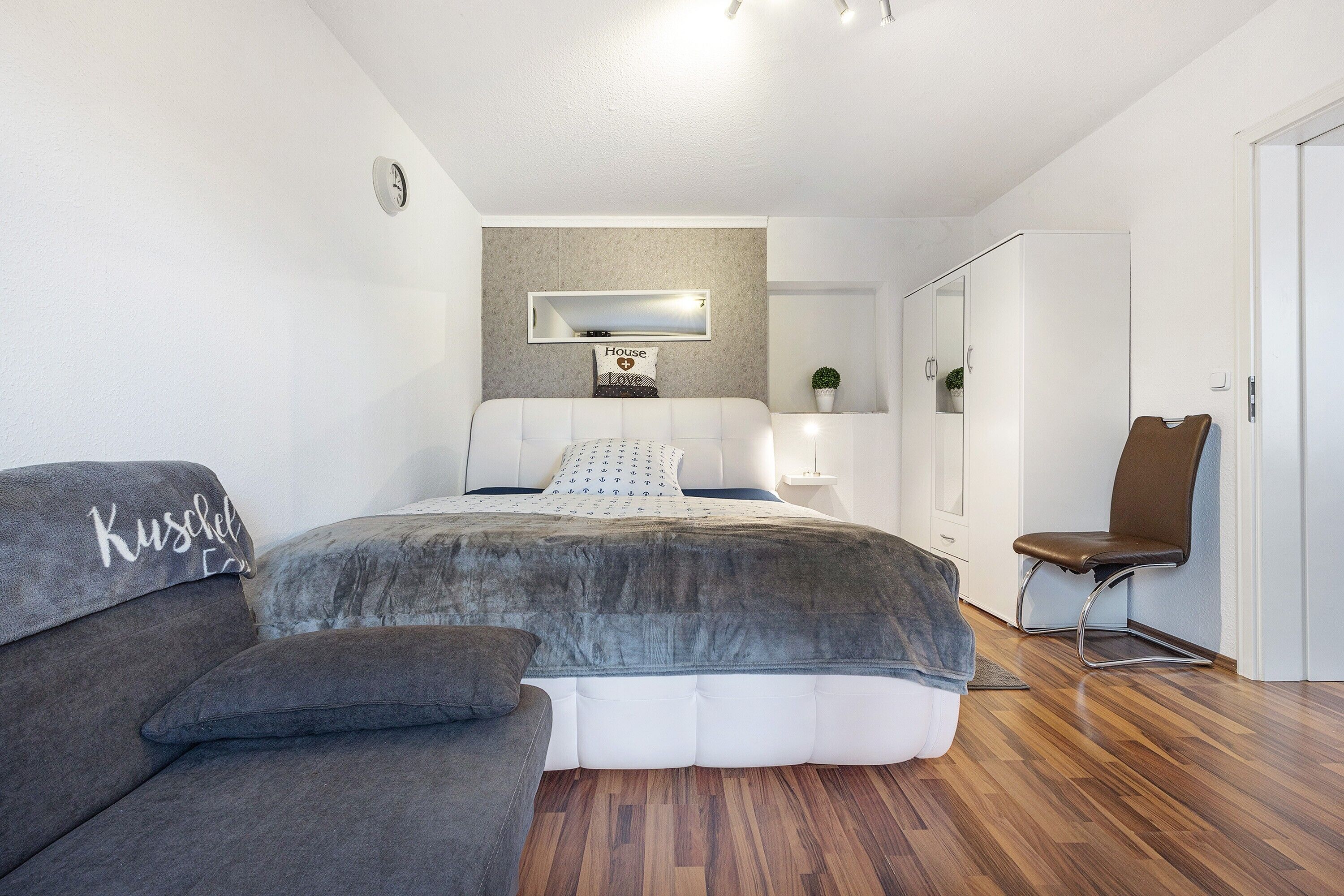 Een slaapkamer met een bed, een bank, een stoel, een spiegel en een kledingkast.