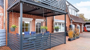 A covered outdoor seating area with a brick wall, metal railing, and potted plants.