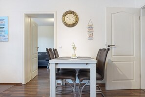 A dining area with a white table, black chairs, a wall clock, and a door.