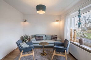 Ein modernes Wohnzimmer mit einer Couch, zwei Sesseln, einem Couchtisch und einer Pendelleuchte.