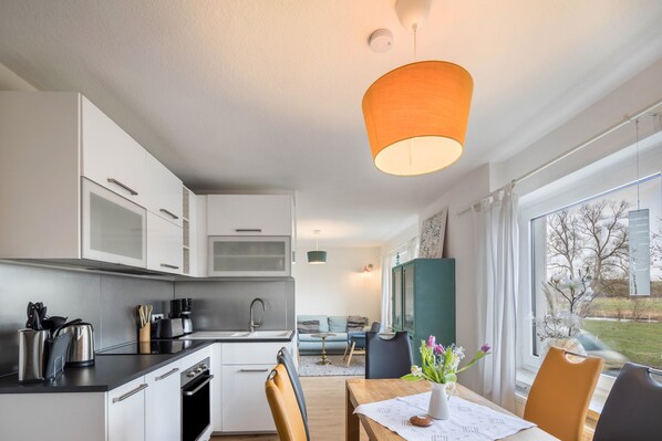 Eine moderne Küche mit weißen Schränken, einer schwarzen Arbeitsplatte und einem Essbereich mit Holztisch und Stühlen.