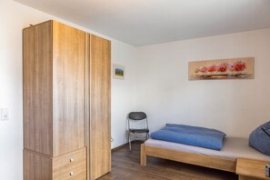Een slaapkamer met een houten garderobe, een enkel bed met een blauwe deken en een schilderij aan de muur.