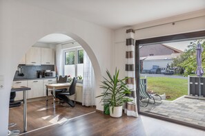 Eine moderne Küche mit Durchgang zu einem Essbereich, einer Topfpflanze und Blick auf einen Garten durch eine Schiebeglastür.