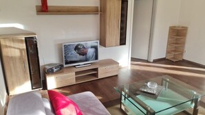 A modern living room with a flat-screen TV, wooden cabinets, a glass coffee table, and a red pillow on the sofa.