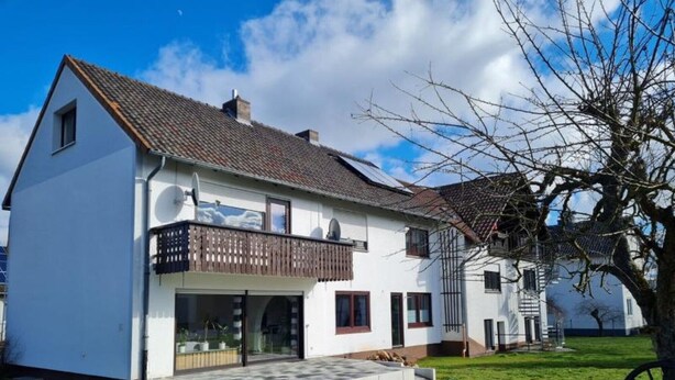 Une maison blanche à deux étages, dotée d’un balcon, d’une antenne parabolique et d’un petit porche à l’avant.