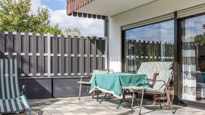 Un espace extérieur aménagé en terrasse, avec une table et des chaises, une clôture en bois et une grande fenêtre.