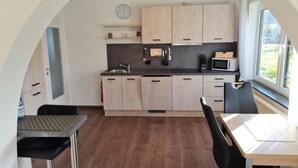 A compact kitchen with a dining area, wooden cabinets, a microwave, and a clock on the wall.