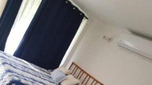 A room with two beds, each with a blue and white patterned bedspread, wooden headboards, and a white air conditioning unit on the wall.